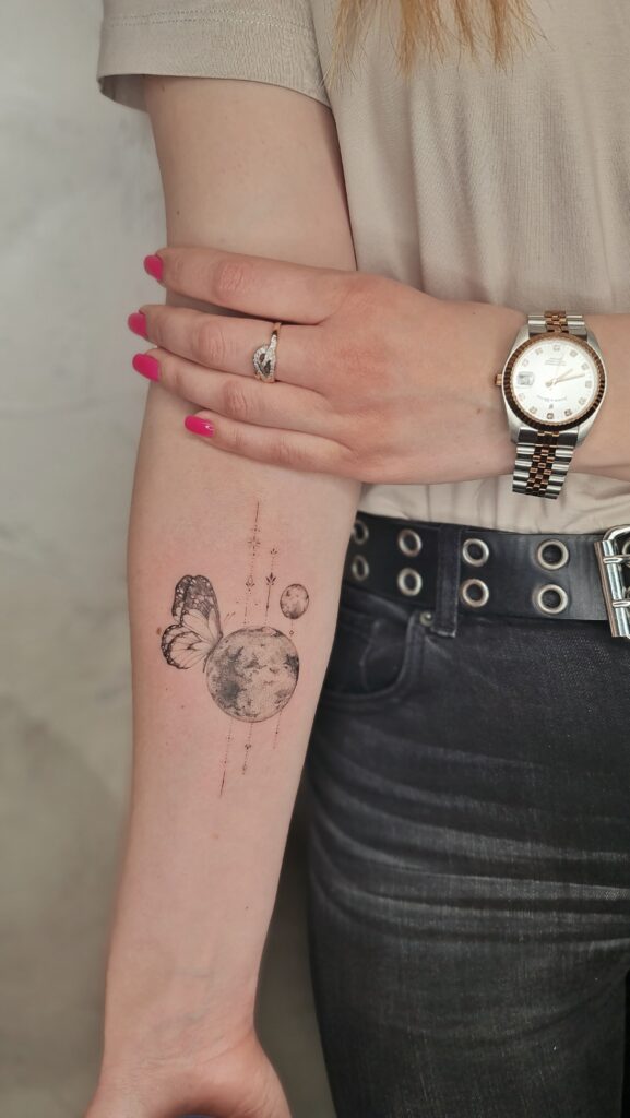 A delicate forearm tattoo merging a half-butterfly with a full moon, connected by fine dotwork and celestial accents.