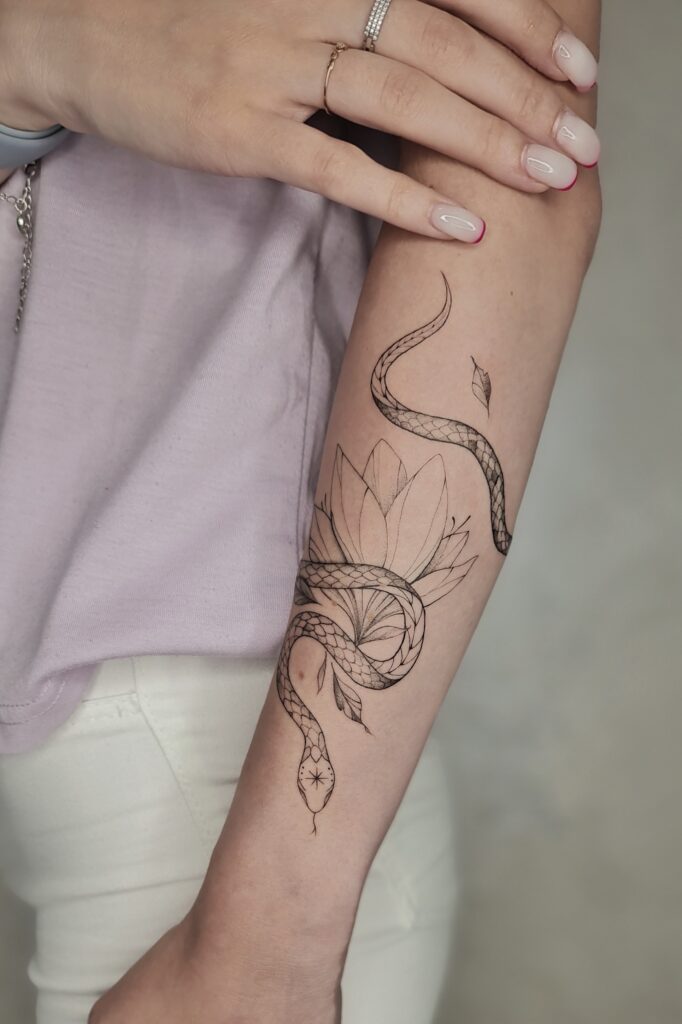 A finely detailed snake winds gracefully through a geometric lotus bloom in this striking forearm piece.
