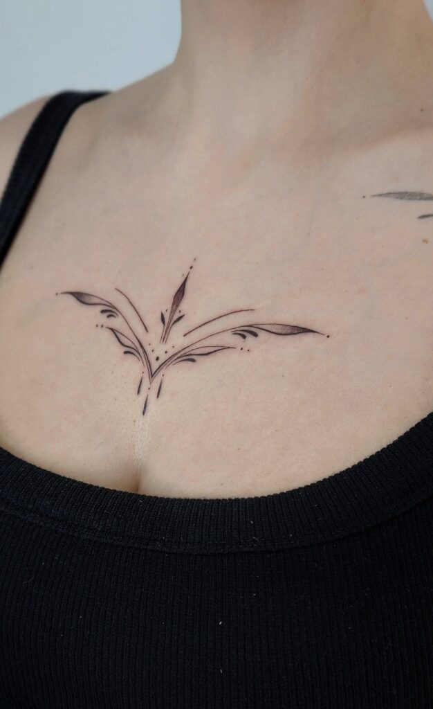 A minimalist fine-line tattoo centered on the collarbone featuring symmetrical leaf sprigs and curling botanical accents that fan outward like delicate wings.